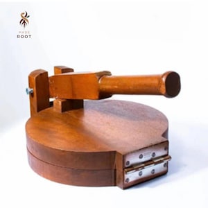 May include: A wooden tortilla press with a round base and a handle. The press is made of a light brown wood and has metal hinges. The logo "MADE ROOT" is in the upper left corner.