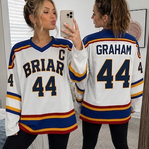 Op de afbeelding: Wit hockey-shirt met blauwe, gele en rode strepen. De voorkant toont "BRIAR", het nummer "44" en de letter "C". De achterkant van het shirt toont de naam "GRAHAM" en het nummer "44".