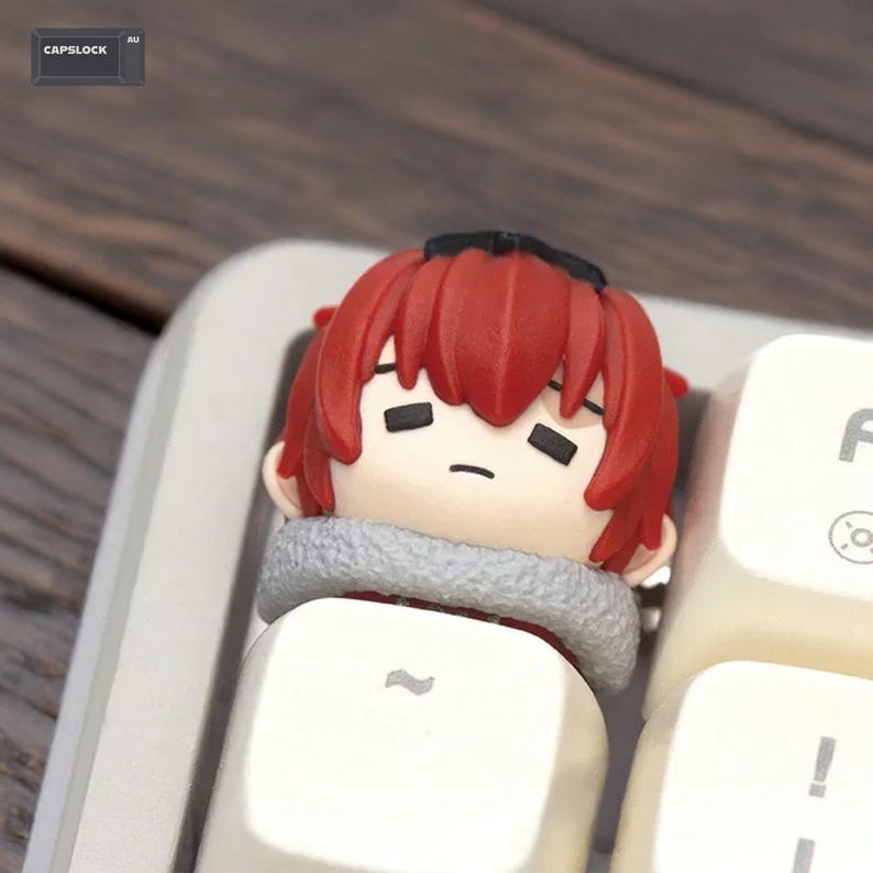 May include: A custom keycap featuring a cartoon character with red hair and a neutral expression. The keycap is designed to fit on a keyboard and is white with a gray trim. The word "CAPSLOCK" is visible in the top left corner.