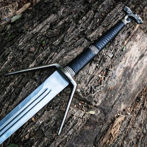 May include: A medieval sword featuring a silver blade and guard, and a black leather-wrapped handle. The sword is displayed on a weathered wooden surface, highlighting its detailed craftsmanship and design.