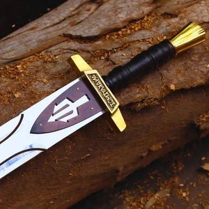 May include: A decorative sword with a white blade and black geometric designs. The hilt is gold and black, with a brown handle. The sword is displayed on a weathered wooden surface, evoking a fantasy or historical setting.