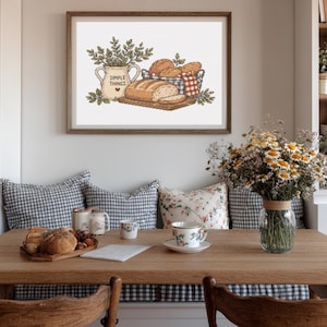 Könnte beinhalten: Ein gerahmter Wandkunstdruck mit einer detaillierten Illustration eines Brotlaibs auf einem Holzbrett, einem Korb mit Brötchen und einem cremefarbenen Krug mit dem Text SIMPLE THINGS und einem kleinen roten Herz, umgeben von grünem Blattwerk.