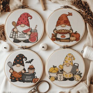 May include: Four circular embroidery hoops featuring gnome illustrations: one with a watermelon and 'SWEET SUMMER' text, one with a pumpkin pie, one with a 'BOO YUMMY' cauldron, and one with lemons and a 'ZEST OF JOY' jar, all on white fabric.