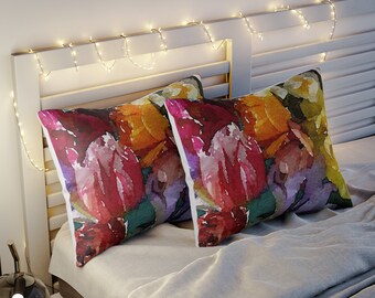 Puede incluir: Dos cojines decorativos rectangulares con un diseño floral en acuarela en tonos rojos, naranjas, amarillos y morados. Descansan sobre una cama con una colcha gris. Luces de hadas adornan el cabecero blanco.