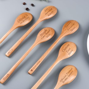 May include: A collection of wooden spoons with engraved text. The spoons feature phrases like "Olivia's 1st Birthday," "Our Morning Ritual," and "Santa's Favorite Spoon." Some spoons have custom text areas, and others include dates and names.