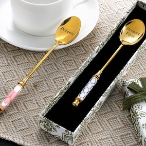 Può includere: Due cucchiaini da dessert dorati, uno con inciso "Delanie", l'altro con "Dessert First". Un cucchiaino ha un manico rosa e bianco, l'altro un manico bianco e blu. Entrambi sono in una scatola decorativa con un cofanetto regalo.