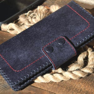May include: A dark navy blue leather wallet featuring a rectangular flap secured by two matching dark navy blue snap buttons. The wallet is constructed with visible thick dark navy blue stitching along the edges and accented with red stitching.
