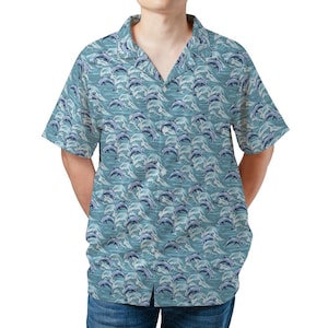 Könnte beinhalten: Kurzärmeliges Hemd mit blauem und weißem Delfinmuster. Das Hemd hat einen klassischen Kragen und eine lockere Passform. Das Design zeigt Delfine, die über Wellen springen und ein maritimes Thema schaffen.