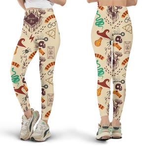 May include: Cream-colored leggings with a repeating pattern of various magical symbols, including a castle, glasses, a key, and a snake. The leggings feature a high waist and are worn with sneakers. The overall design has a whimsical and fantasy theme.