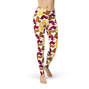 Può includere: Leggings bianchi con un motivo ripetuto di cani dei cartoni animati nei toni del marrone, giallo e bordeaux. I leggings sono aderenti e a vita alta, adatti per attività sportive o per il tempo libero.
