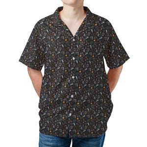May include: Black button-down shirt with a colorful, all-over pattern. The short-sleeved shirt features a classic collar and a series of small, white buttons down the front. The pattern includes various graphic elements in white, green, red, and yellow.