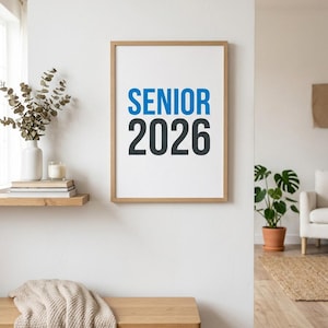 Peut inclure: Un cadre avec l'inscription "SENIOR 2026" en bleu et noir. L'impression est affichée sur un mur blanc. Un banc en bois avec une couverture beige est au premier plan. Une étagère avec un vase et une bougie est visible.