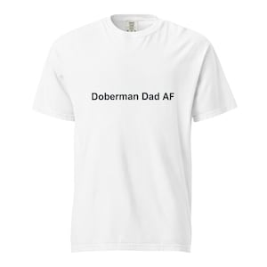 Può includere: T-shirt bianca con la scritta "Doberman Dad AF" stampata in nero. La maglietta è a maniche corte, girocollo, realizzata in un materiale morbido e confortevole. La maglietta è un capo casual.