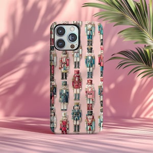 Puede incluir: Una funda de teléfono con un patrón repetido de cascanueces de juguete en varios colores, incluyendo rojo, azul y rosa. La funda tiene un acabado brillante y un recorte para la cámara.