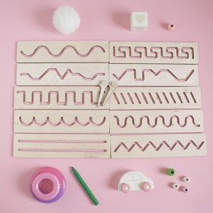 May include: A set of ten rectangular wooden tracing boards featuring various engraved patterns including waves, zigzags, and straight lines. The set includes two small wooden styluses, a white pom-pom, a heart cube, a green pencil, and a small toy car.