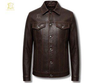 May include: A dark brown leather jacket featuring a classic collar, a front button-down closure with metallic buttons, two chest pockets with buttoned flaps, and vertical seam detailing. A small logo emblem is visible on the upper chest area.