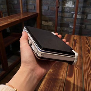 May include: A black and white phone case with a textured black top and a white frame. The case has a sleek design and is held in a hand, showcasing its form and details. The case is designed to protect a phone.