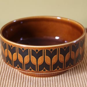 May include: A brown ceramic bowl with a decorative black and tan pattern around the exterior. The bowl has a rounded shape and a glossy finish, suitable for serving food or as a decorative piece.