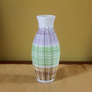 Puede incluir: Un jarrón de cerámica con cuello estrecho y cuerpo redondeado que presenta bandas horizontales en lavanda, verde claro y bronceado. La superficie está decorada con un patrón repetitivo de líneas verticales negras y pequeños guiones blancos sobre las secciones.