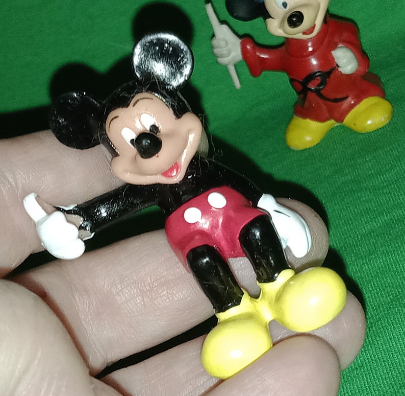 Pode incluir: Uma figura de pl&aacute;stico do Mickey Mouse preta e vermelha com sapatos amarelos. A figura est&aacute; levantando a m&atilde;o direita no ar.
