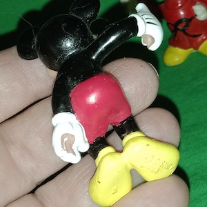 Pode incluir: Uma figura de pl&aacute;stico do Mickey Mouse preta e vermelha com sapatos amarelos. A figura est&aacute; levantando o bra&ccedil;o direito e tem uma luva branca na m&atilde;o direita.