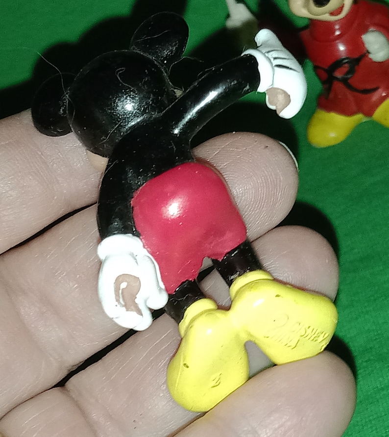 Pode incluir: Uma figura de pl&aacute;stico do Mickey Mouse preta e vermelha com sapatos amarelos. A figura est&aacute; levantando o bra&ccedil;o direito e tem uma luva branca na m&atilde;o direita.