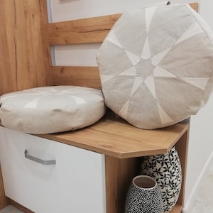 Può includere: Una panca in legno con una seduta imbottita bianca e due cuscini decorativi. La panca ha un armadio bianco con una maniglia argentata e uno scaffale con due vasi in bianco e nero.