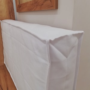 Puede incluir: Funda de tela blanca para una unidad de aire acondicionado. La funda está hecha de una tela blanca suave y tiene un diseño simple.