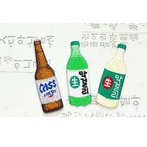 May include: Embroidered patches of three beverage bottles. One is brown with "Cass Fresh" text, another is green with Korean text and a green cap, and the third is white with Korean text and a green cap.