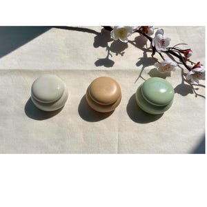 Puede incluir: Una taza de cerámica blanca con un asa negra y el texto "But First, Coffee" en un estilo manuscrito. La taza está sobre una superficie blanca. La taza es probablemente para bebidas calientes.