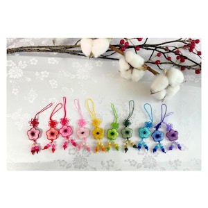 Pode incluir: Uma coleção de ornamentos coloridos em forma de flor, feitos à mão. Cada ornamento apresenta um esquema de cores diferente, incluindo vermelho, rosa, amarelo, verde, azul e roxo. São adornados com detalhes de contas e laços para pendurar.