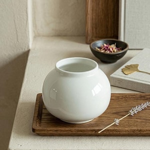 May include: A white ceramic mug with a black handle and the text "But First, Coffee" in a black, handwritten-style font. The mug is on a white surface.