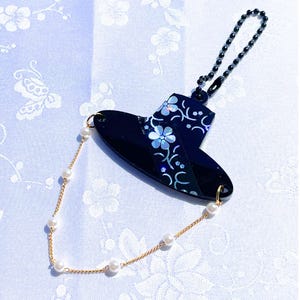 May include: A black accessory with a floral design and a gold chain with pearls. The accessory has a black chain and a gold chain with pearls. The floral design has white and light blue accents.
