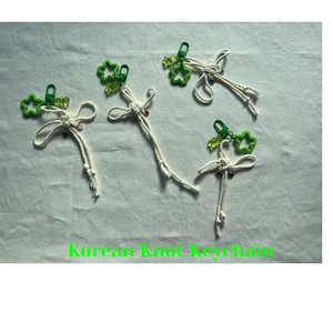 May include: Five handmade Korean knot keychains. Each keychain has a cream-coloured knotted cord, a green star-shaped charm, and small colourful beads. The text "Korean Knot Keychain" is at the bottom of the image.