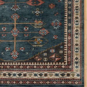 May include: A section of a teal-colored rug with an intricate, traditional design. The rug features a central field with floral and geometric patterns in shades of orange, blue, and brown, framed by a detailed border.