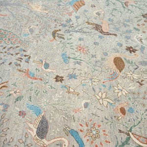 以下が含まれることがあります： 鳥、花、葉の模様が施された、明るい青色のラグ。茶色、青、赤の色合いの様々な鳥類が、花の要素を背景に描かれています。
