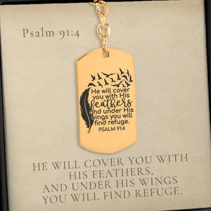 May include: A gold-toned dog tag pendant necklace featuring a black engraved feather and bird design with the text Psalm 91:4, He will cover you with His feathers, and under His wings you will find refuge, presented in a black gift box.