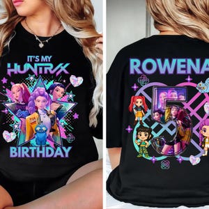 May include: Black graphic t-shirt with the text "IT'S MY HUNTRAX BIRTHDAY" on the front. The design features cartoon characters in a star shape with hearts and stars. The back of the shirt says "ROWENA 5".