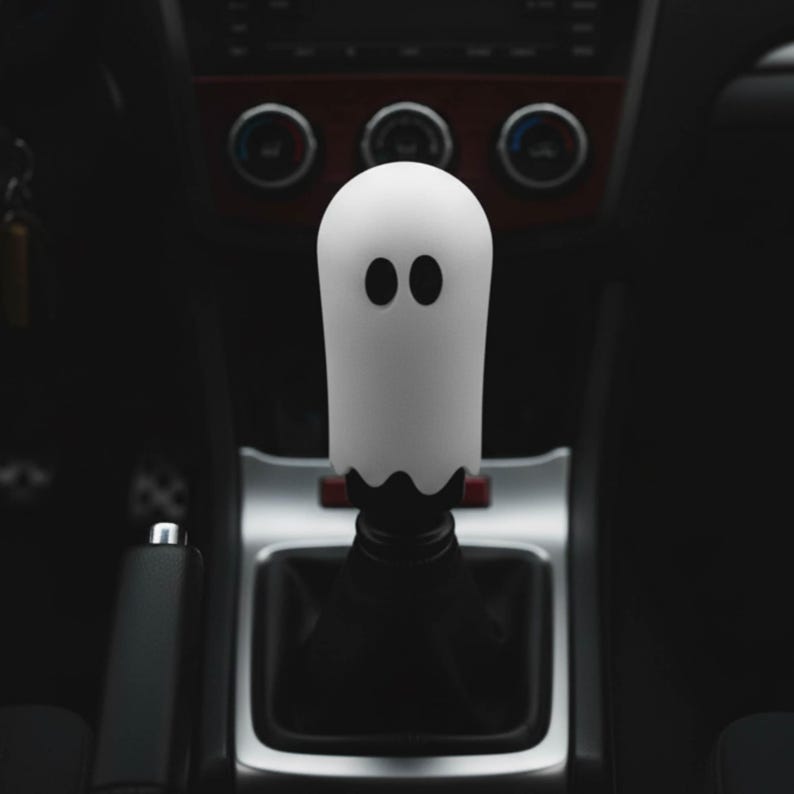 White ghost weighted shift knob on a manual transmission gear shifter in a dark car interior, cute Halloween JDM shift knob and custom gear shifter knob for 6 speed cars, manual shift knob upgrade for drift builds, stance cars and hot rods, unique gear knob for sim racing cockpit, iRacing rig or gaming simulator setup, funny spooky car accessory for modified JDM interiors and tuners.