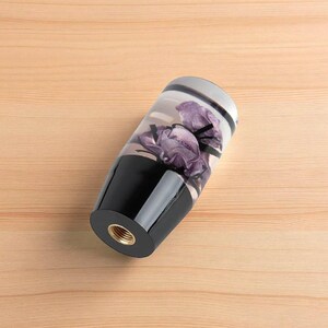 Close up of purple rose resin shift knob lying on its side showing threaded metal insert, custom shift knob for manual transmission gear shifter, clear resin body with embedded purple flowers, weighted gear knob compatible with 6 speed cars, ideal for sim racing, iRacing cockpit and gaming simulator shifter upgrades.
