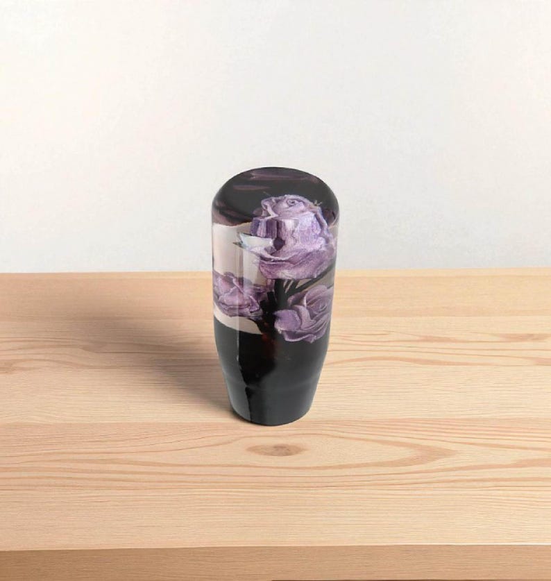 Front view of purple roses resin shift knob 4 inch tall on wooden table, clear acrylic flower shift knob with three detailed violet roses inside, weighted shift knob design for smooth gear changes, universal manual transmission shifter knob for JDM cars, hot rods, custom builds and sim racing gear shifter setups.