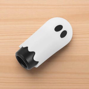 Side view of the ghost shift knob resting on a wooden surface, highlighting its rounded shape and hand-polished resin finish. The playful ghost design makes it stand out in any car interior, from JDM builds to drift and racing setups. This 3.4-inch knob offers smooth handling, enhanced control, and a creative custom touch.