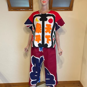 May include: A two-piece outfit consisting of a short-sleeved top and matching pants. The top features a red, black, and white design with yellow moon and red sun graphics, displaying the Japanese characters 天下泰平. The pants are maroon with large blue and white floral-like patterns.