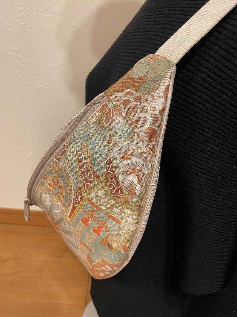 May include: A patterned fanny pack with a cream-coloured strap. The bag features a floral design in shades of brown, orange, and blue. The zipper is silver. The bag is worn across the body.