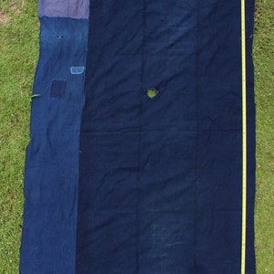 Könnte beinhalten: Ein großes indigo-blaues Stoffpaneel mit einem kleineren indigo-blauen Paneel, das an der linken Seite angenäht ist. Der Stoff hat einen abgenutzten und verblassten Look mit mehreren Löchern und Flicken.