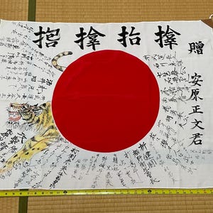 Peut inclure: Un drapeau rectangulaire blanc avec un grand cercle rouge au centre, une illustration de tigre sur la gauche et des calligraphies japonaises noires. Un mètre ruban jaune indique que le drapeau mesure environ 91 cm de large et 71 cm de haut.