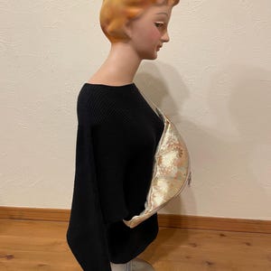 May include: A black, off-the-shoulder sweater on a mannequin. A gold and cream-coloured floral patterned bag is draped over the mannequin's shoulder. The mannequin has a vintage look with blonde hair and a pale complexion.