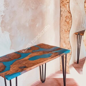 Puede incluir: Mesa de madera artesanal con borde natural y río de resina epoxi azul. Patas de horquilla negras sostienen la mesa. El texto "kartik handicrafts" es visible. Un mueble decorativo y único.