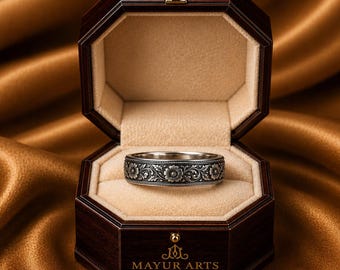 May include: A silver ring with a floral design is displayed in an open, dark wooden octagonal jewellery box. The ring has detailed flower and leaf patterns. The box's interior is beige. The logo "MAYUR ARTS - JEWELRY" is printed on the box.