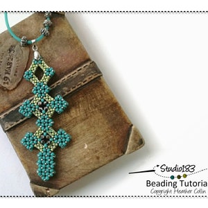 May include: A teal and green beaded pendant in the shape of a cross, hanging from a teal cord. The pendant is on a brown leather-bound book with the text "19 MAR 1917" visible.